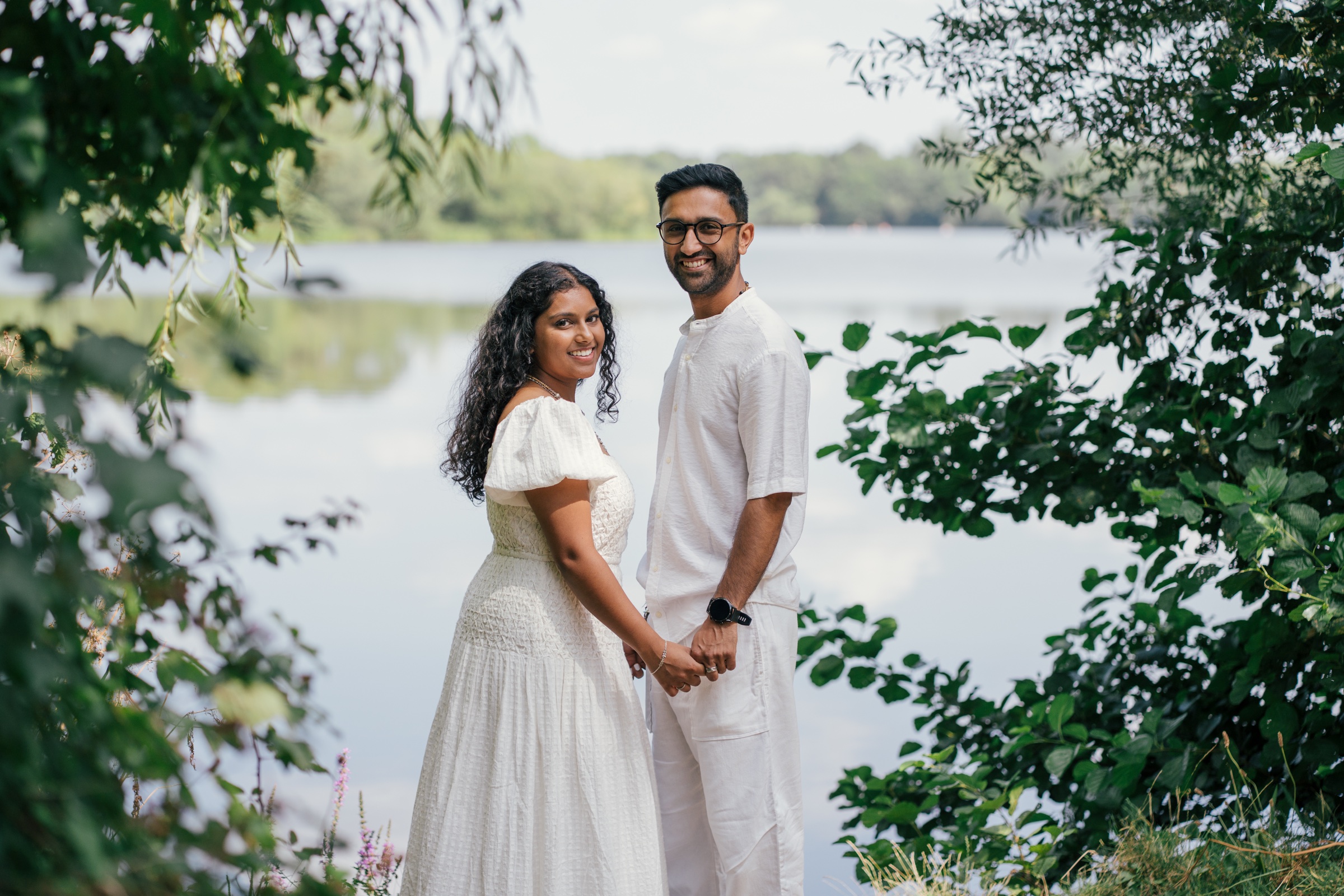 A couple dressed in white beside a lake